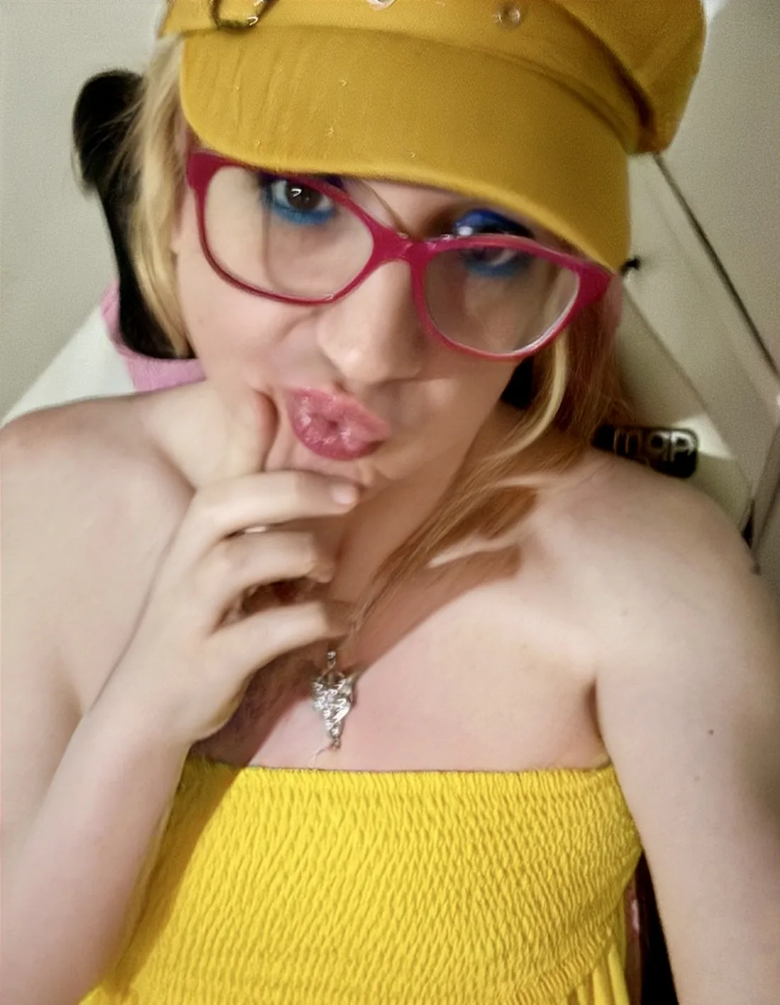 Catie in pink glasses, blue eye makeup, and a yellow cap
